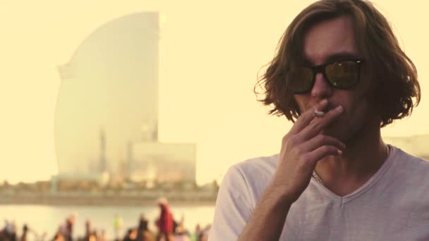 Молодой белый мужчина с длинными волосами курит сигарету — стоковое видео