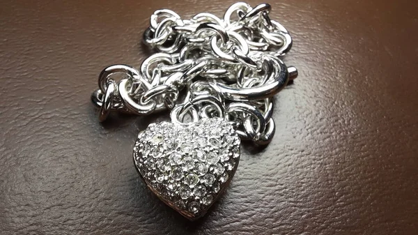 Heart-shaped chrome bracelet with inlayed crystals and with a chain of rings.