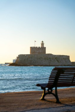 Mandraki Limanı 'ndaki Aziz Nicholas Kalesi ve gün batımında deniz kenarı koltuğu .