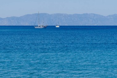 Arka plandaki dağlarda, okyanusta yelkenli tekneler..