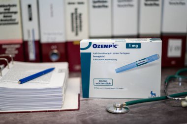 Tip 2 diyabet ve uzun vadeli ağırlık yönetimi tedavisi için semaglutid içeren bir Ozempic uyuşturucu kutusu bir masada ve arka planda farklı tıp kitapları.