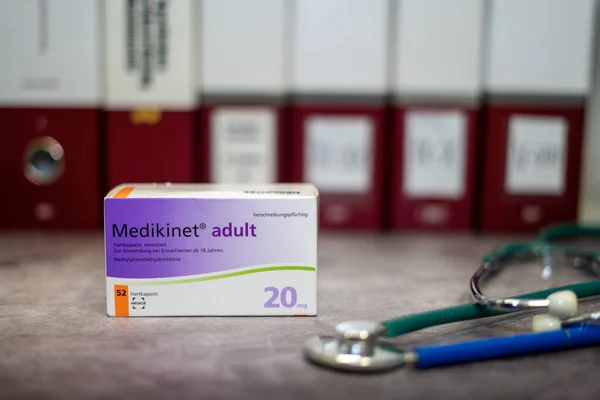 Dikkat eksikliği hiperaktivite bozukluğunun tedavisi için metilfenidat içeren bir ilaç kutusu (ADHD) masanın üzerinde ve arka planda farklı tıp kitapları bulunmaktadır..