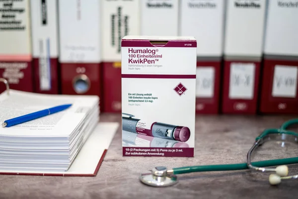Tip 1 ve tip 2 diyabet tedavisi için insülin lisproyu içeren Humalog KwikPen bir masada ve arka planda farklı tıp kitapları bulunmaktadır..