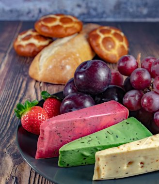 Dutch cheese types on plate and bread and fruit on wooden backdrop