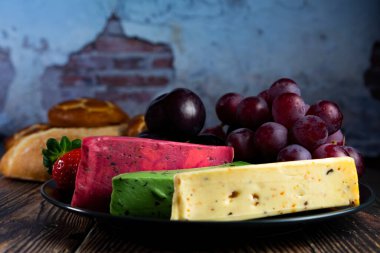 Dutch cheese types on plate and bread and fruit on wooden backdrop