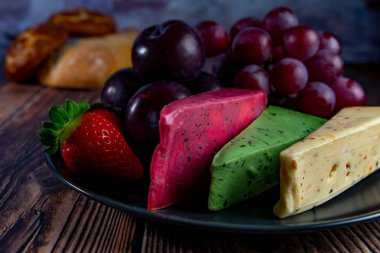 Dutch cheese types on plate and bread and fruit on wooden backdrop