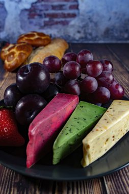 Dutch cheese types on plate and bread and fruit on wooden backdrop