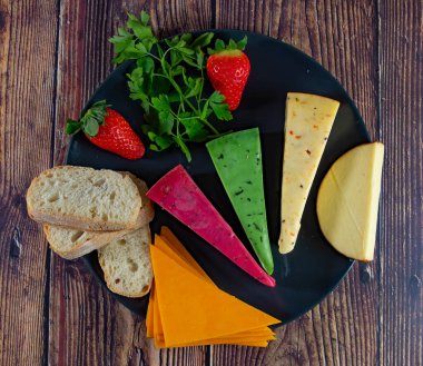 Dutch cheese types on plate and bread and fruit on wooden backdrop.Top view