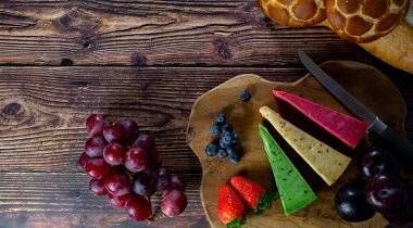 Dutch cheese types on plate and bread and fruit on wooden backdrop.Top view