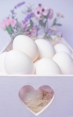 Beyaz renkli kalp önde ve beyaz yumurtalar ve arka planda bulanık çiçekler Paskalya veya yiyecek konsepti