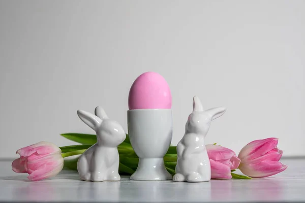 带有粉色复活节彩蛋和瓷制复活节兔子的瓷制彩蛋杯和相同的彩色粉红白色郁金香 背景为白色 — 图库照片