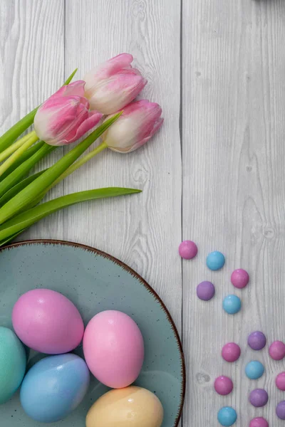彩色复活节彩蛋和彩色巧克力软糖 蓝色盘子和粉色白色郁金香 白色木制背景 — 图库照片
