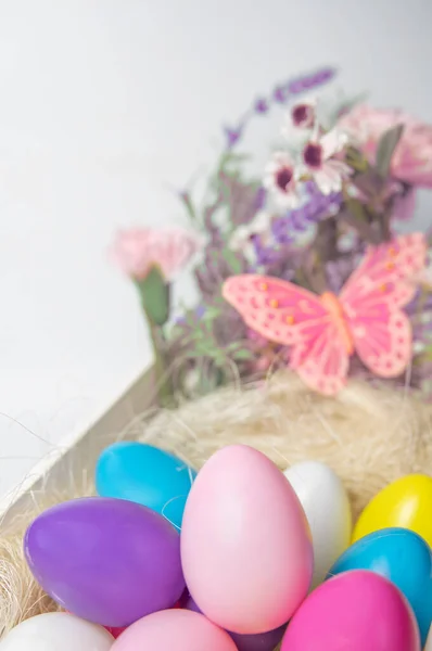 色彩艳丽的复活节彩蛋和花朵装在木制的白色盒子里 白色背景上有粉色蝴蝶 — 图库照片