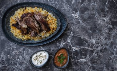 Kabsa pilavı ve ızgara kuzu ve iki küçük tabak yoğurt ve acı sos..