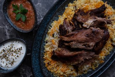 Kabsa pilavı ve ızgara kuzu ve iki küçük tabak yoğurt ve acı sos..