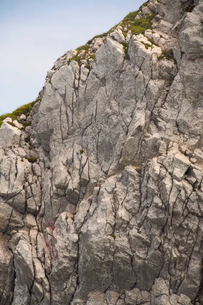 Dağın kenarında mavi bir gökyüzü ve çimenli bir arazi. Taş katmanlı..