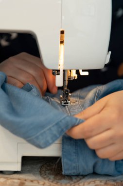 Evde dikiş makinesiyle elbise dikip tamir eden bir kadın.