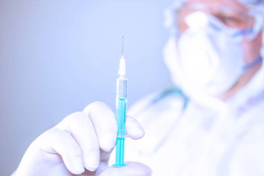 Cerrahi maske takan ve ameliyat eldiveni takan bir doktor beyaz arka planda iğne ya da aşı yapmak için elinde iğne tutuyor. 