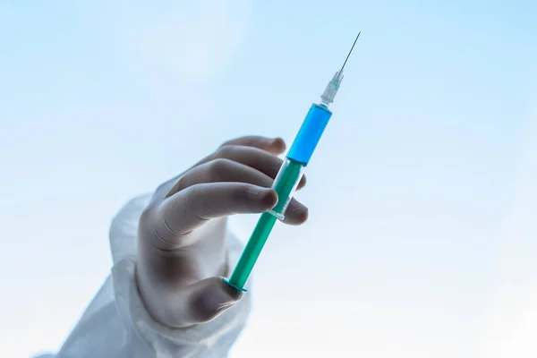 Syringe for injection, Doctor wearing surgical gloves holding a needle or syringe for injection with a blue liquid against white blue background.