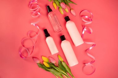 Güzellik makyaj şişelerinin maketi cilt sağlığı ürünleri pembe arka planda laleler.