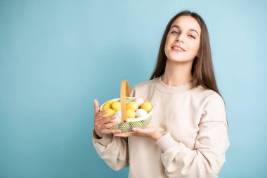 Şirin esmer kadın, elinde Paskalya yumurtalarını tutuyor. Stüdyoda, mavi arka planda..