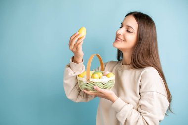 Şirin esmer kadın, elinde Paskalya yumurtalarını tutuyor. Stüdyoda, mavi arka planda..