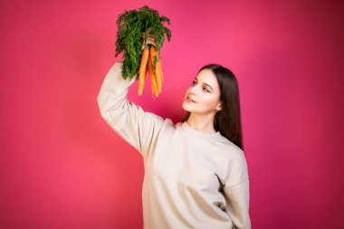 Elinde taze havuç tutan mutlu, genç bir kız. Pembe arka plan. Sağlıklı beslenme kavramı.