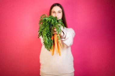 Genç mutlu kız taze havuç tutuyor. Pembe arka plan. Sağlıklı beslenme kavramı.