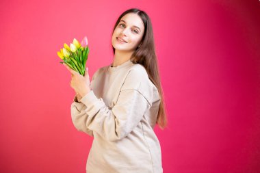 Mutlu genç kadın pembe arka planda bir buket lalenin tadını çıkar..