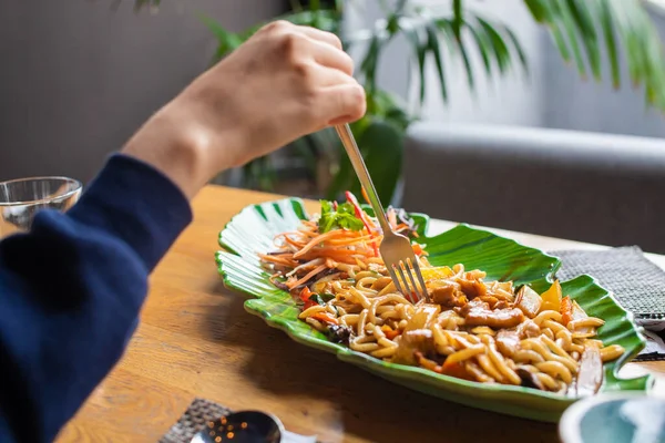 Soba, udon, yeşil tabakta tavuk ve sebzeli Asya buğday eriştesi. Kadınlar çatalla yer.