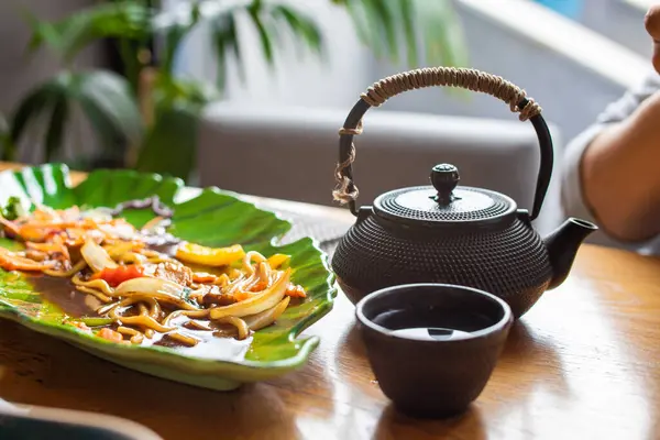 Soba, udon, yeşil tabakta tavuk ve sebzeli Asya buğday eriştesi çaydanlık ve çay fincanı.