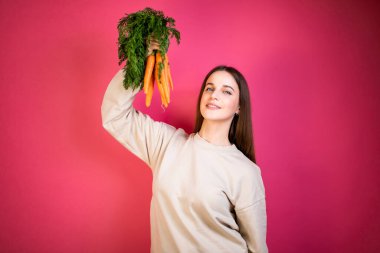 Genç mutlu kız taze havuç tutuyor. Pembe arka plan. Sağlıklı beslenme kavramı.