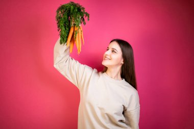 Genç mutlu kız taze havuç tutuyor. Pembe arka plan. Sağlıklı beslenme kavramı.