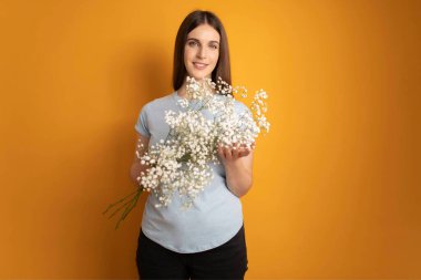 Çekici, neşeli, hayalperest bir kızın portresi elinde çiçekli, sarı renkli arka plan. Yüksek kalite fotoğraf