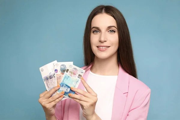 Beautiful young woman holding united kingdom pounds banknotes looking positive and happy standing and smiling with a confident smile . High quality photo