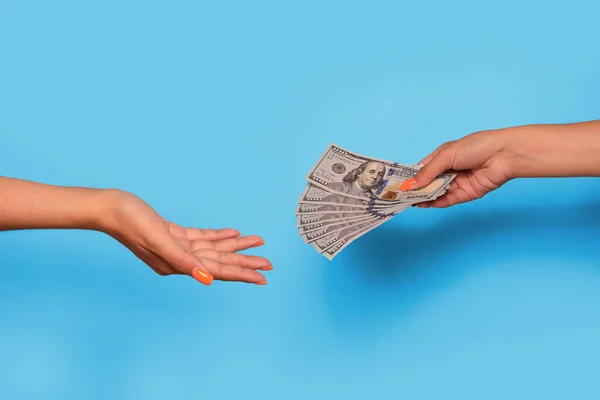 Hand giving dollar currency and hand take, over blue background. Giving money to help. High quality photo