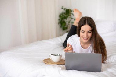 Genç Millennial Kızı Dizüstü bilgisayar kullanarak yatakta yatıyor. Evden çalışıyorum. Yüksek kalite fotoğraf