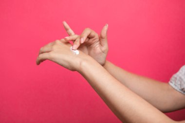 Kadın, pembe arka planda izole edilmiş ellerine krem sürüyor. Yüksek kalite fotoğraf