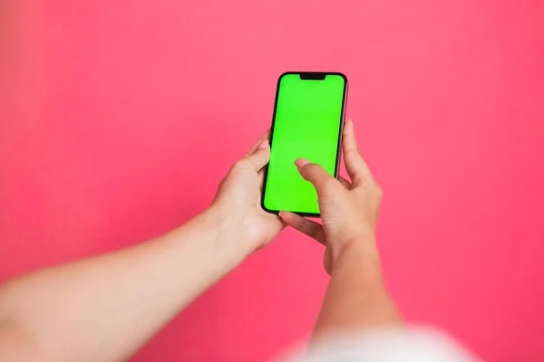 Woman hand Holding a Green Screen Smartphone scroll and touch display on pink background. High quality photo