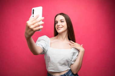 Portrait of a smiling cute woman making selfie photo on smartphone on a pink background. High quality photo