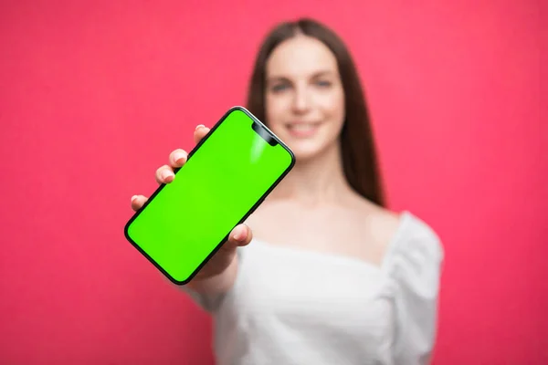 Mutlu kadın ayakta duruyor ve telefonu pembe arka planda tutuyor. Yeşil ekran telefon ekranı. Yüksek kalite fotoğraf