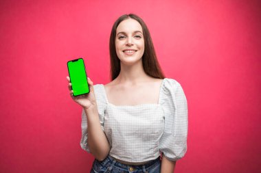 Happy woman standing and hold smartphone on pink background. Green screen phone screen. High quality photo