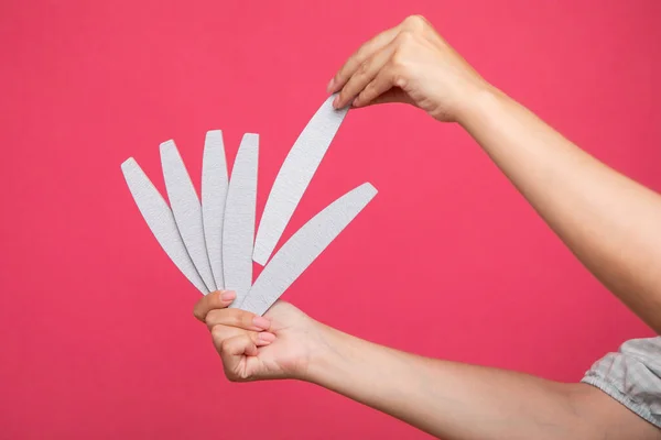 Set of nail files in woman hand and choosing one of them on pink background. Manicurist equipment. High quality photo