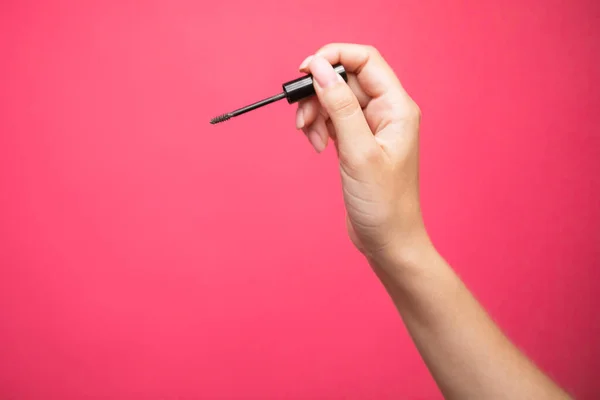 Close up of womans hand holding an eyebrows brush mascara on pink background. High quality photo