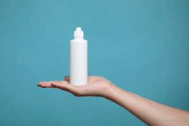 A bottle of liquid for lenses in woman hand on a blue background. Mock up of liquid for lenses. High quality photo