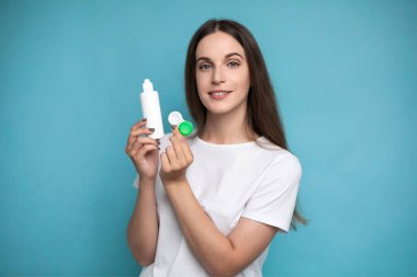 Young woman with contact lenses and bottle of solution on color background. High quality photo