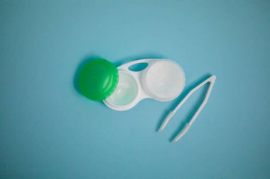 Case with contact lenses and tweezers on light blue background. High quality photo