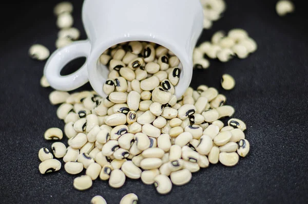 Black eyed beans pouring from a mug on a black background,  dried kidney beans on a black background