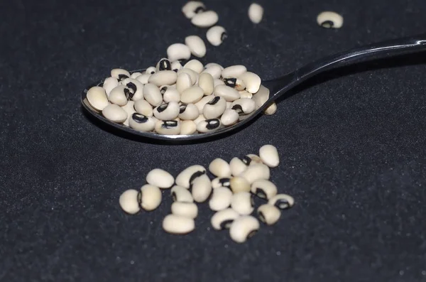 Dried black eyed bean in a tablespoon spilled on black background. Selective focus,  dried kidney beans on a black background