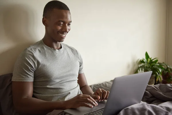 Młody Afrykanin Przeglądający Internet Laptopem Siedząc Rano Swoim Łóżku Domu — Zdjęcie stockowe